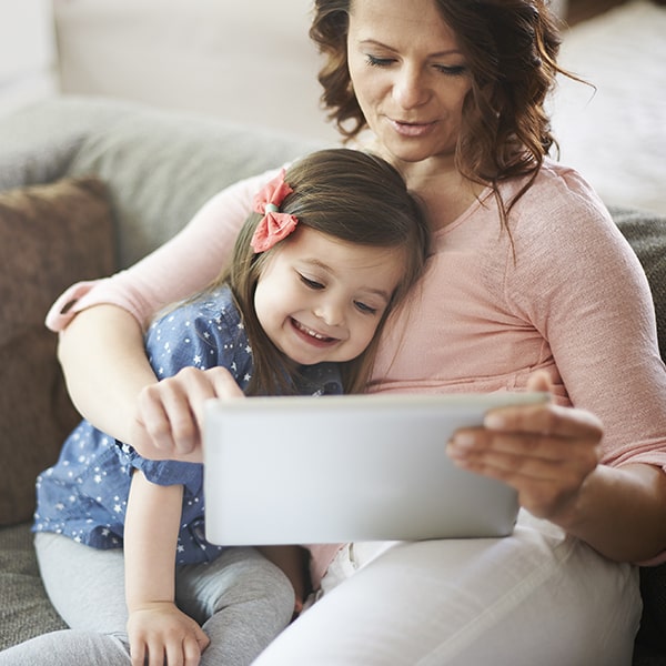 A mother and her daughter sitting on the sofa while looking at a tablet